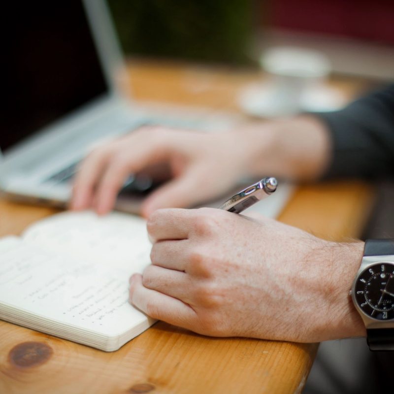Man writing in a note pad with a laptop